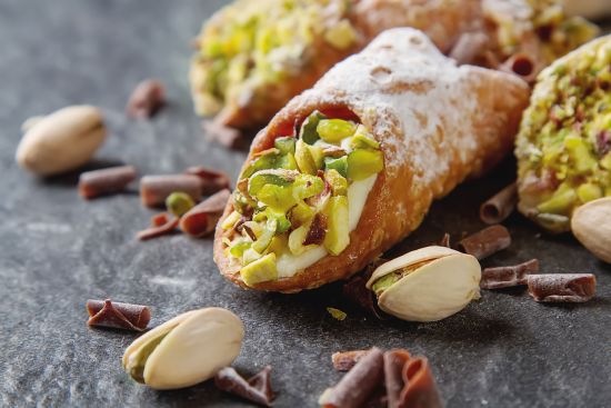 green gold pistachios decorate a rich, ricotta-filled canoli, a staple treat in Sicily